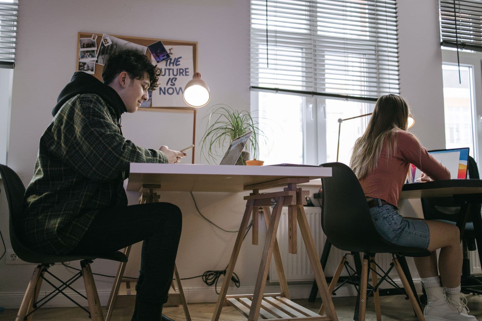 Two coworkers each working on a laptop at a shared desk in a small studio office