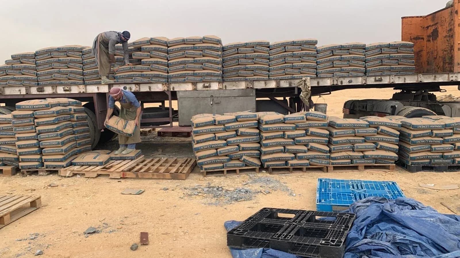 Workers unload bags of cement from a flatbed truck at a construction site in Saudi Arabia